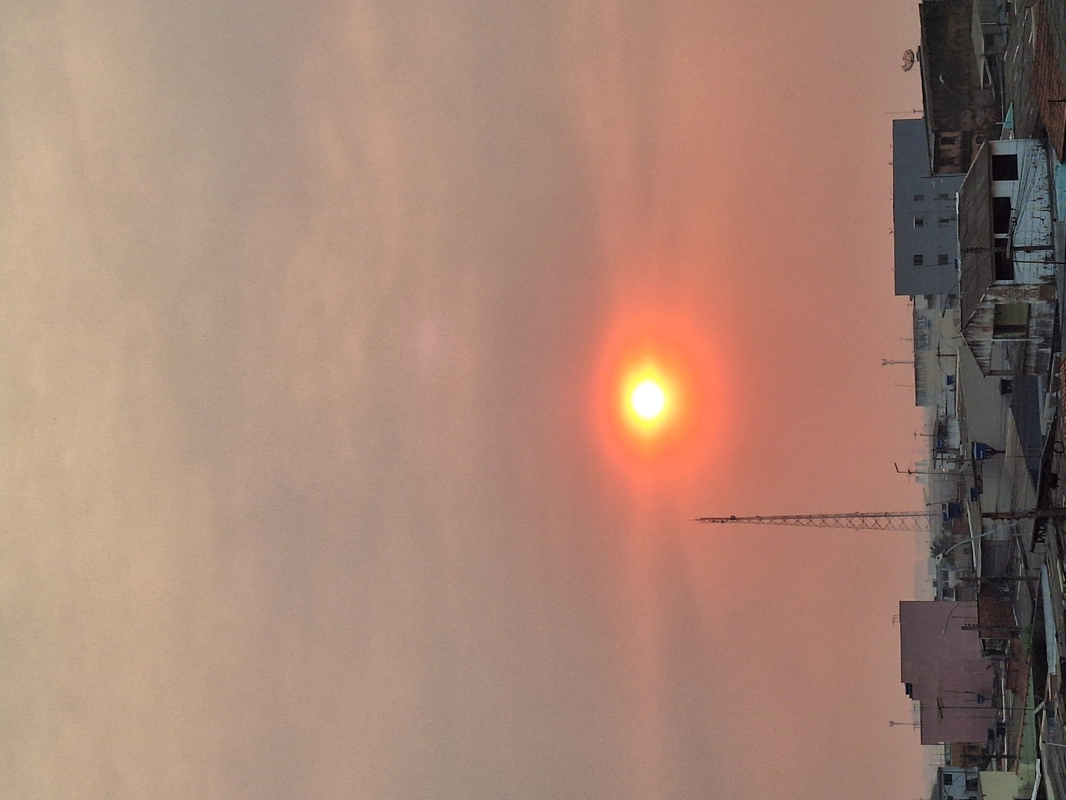 Imagem de um céu repleto de fumaça, com o sol parcialmente obstruído ao centro, sua luz amarela alaranjada atravessando a fumaça.