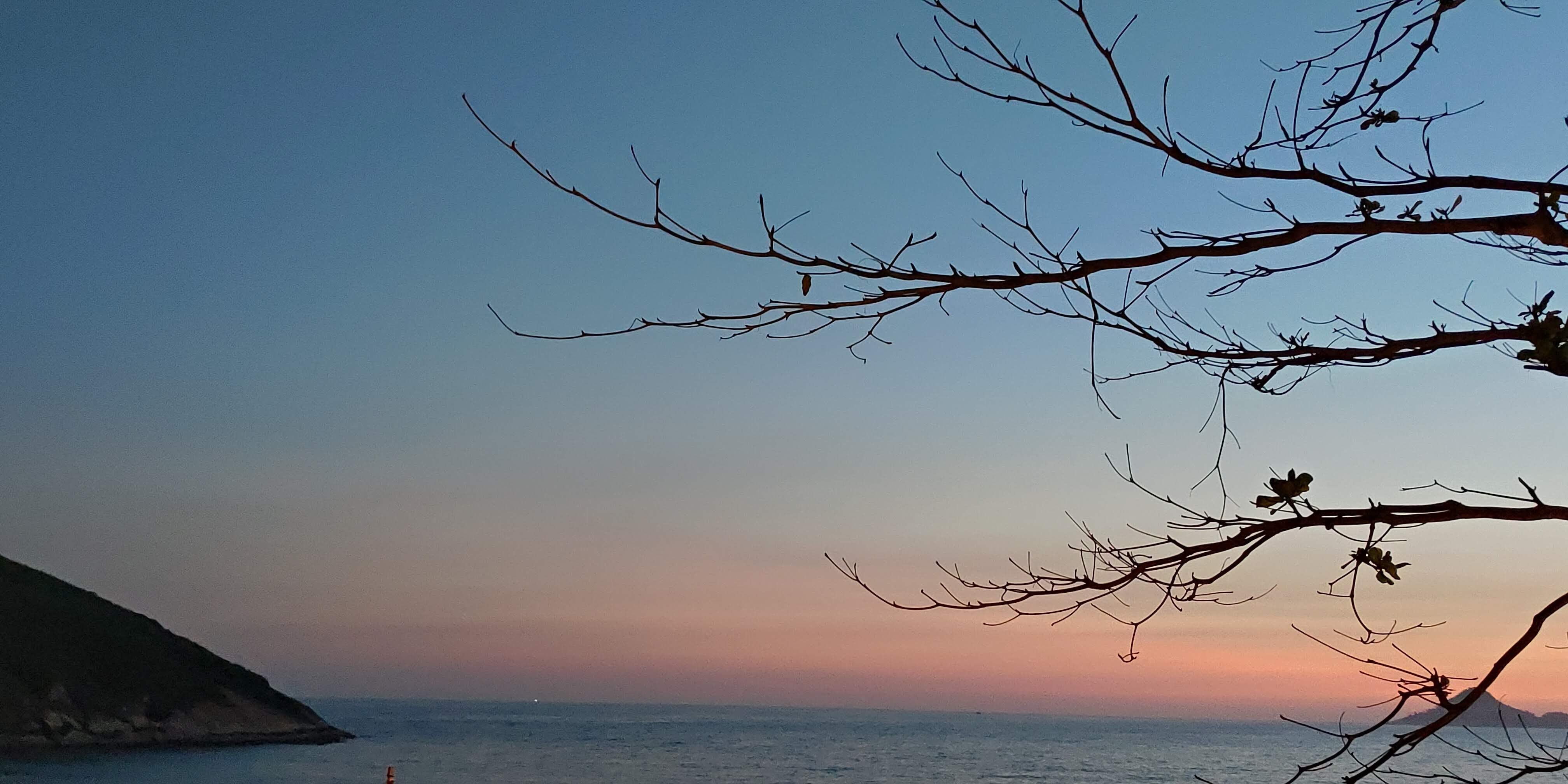  A fotografia foi tirada por mim em frente a praia da macumba e a Pedra do Pontal. Vê-se em primeiro plano galhos secos de uma ávore com pouquíssimas folhas, no canto oposto, parte da Pedra do Pontal, ao fundo um céu azul e vermelho característico de quando o sol se põe, que toca o mar. 